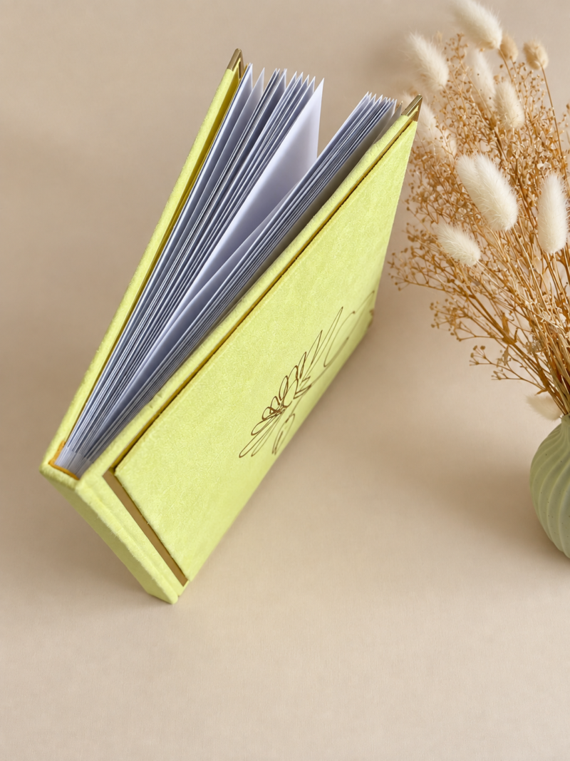 Kollane sametine fotoalbum valgete lehtede, kuldsete nurgakaitsmete ja minimalistliku lillemustriga kaanel.